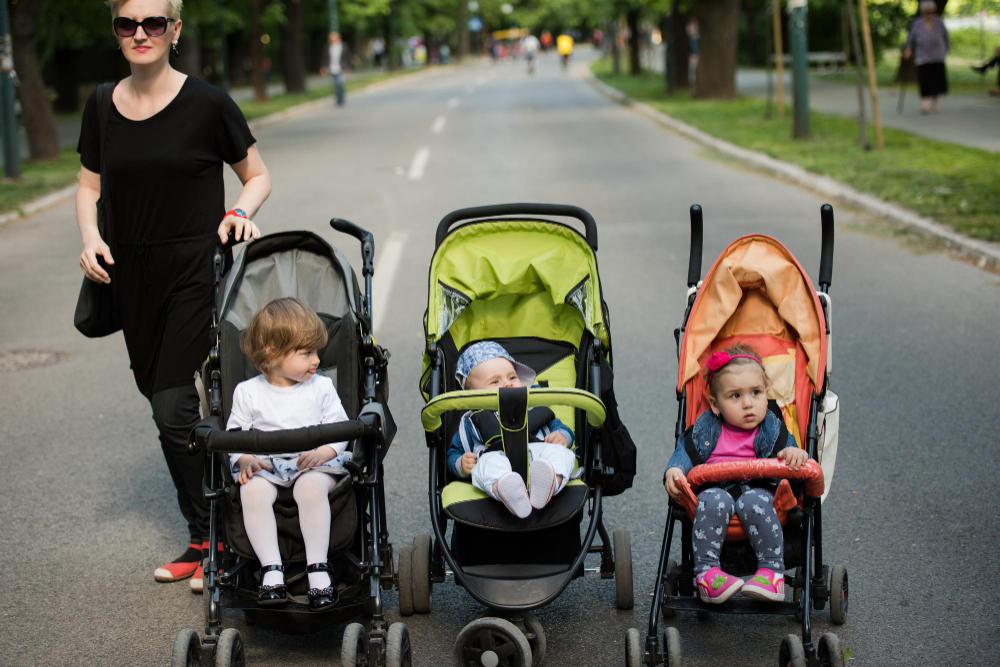 Tres sillas de paseo con niños en una calle arbolada