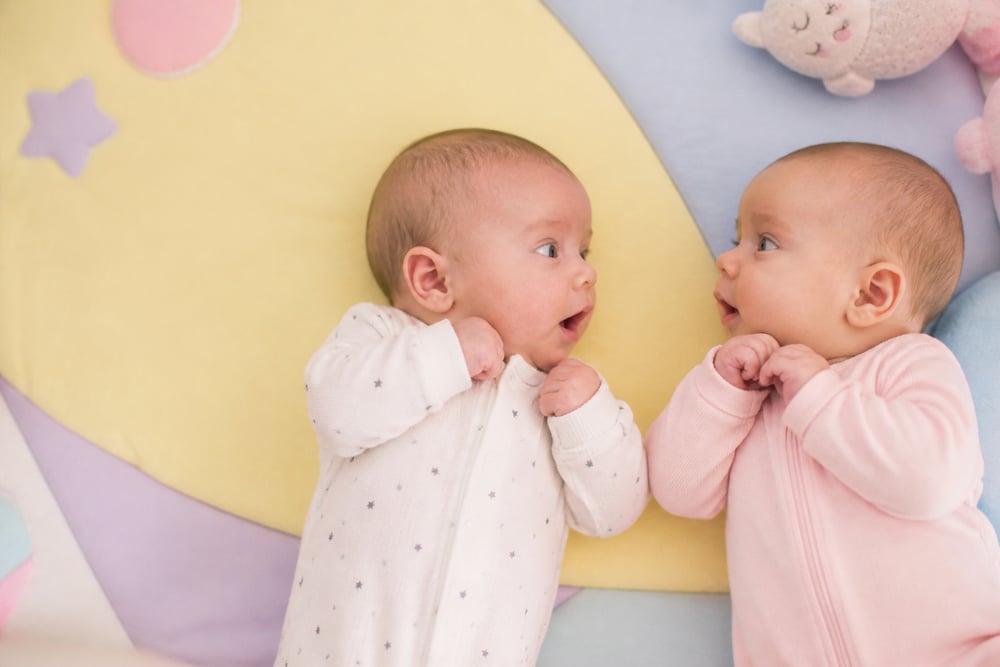Two newborn babies looking at each other on a soft pastel blanket.